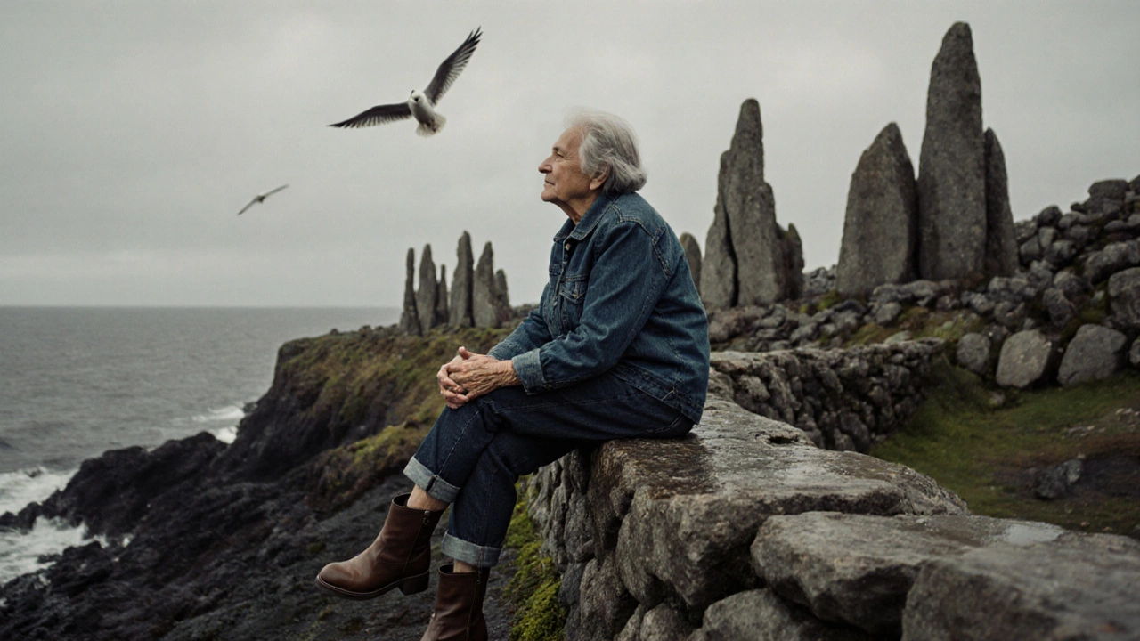 An older woman sitting on a stone wall at Giant’s Causeway, wearing cropped denim jeans and watching birds in the rain.
